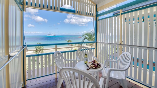 A balcony with a white railing, a table with chairs, and a view of the ocean and beach. - Tangalooma Island Resort (Moreton Island)