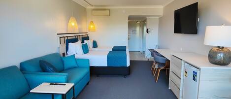 A hotel room with a bed, a desk, a chair, a sofa, and a TV.