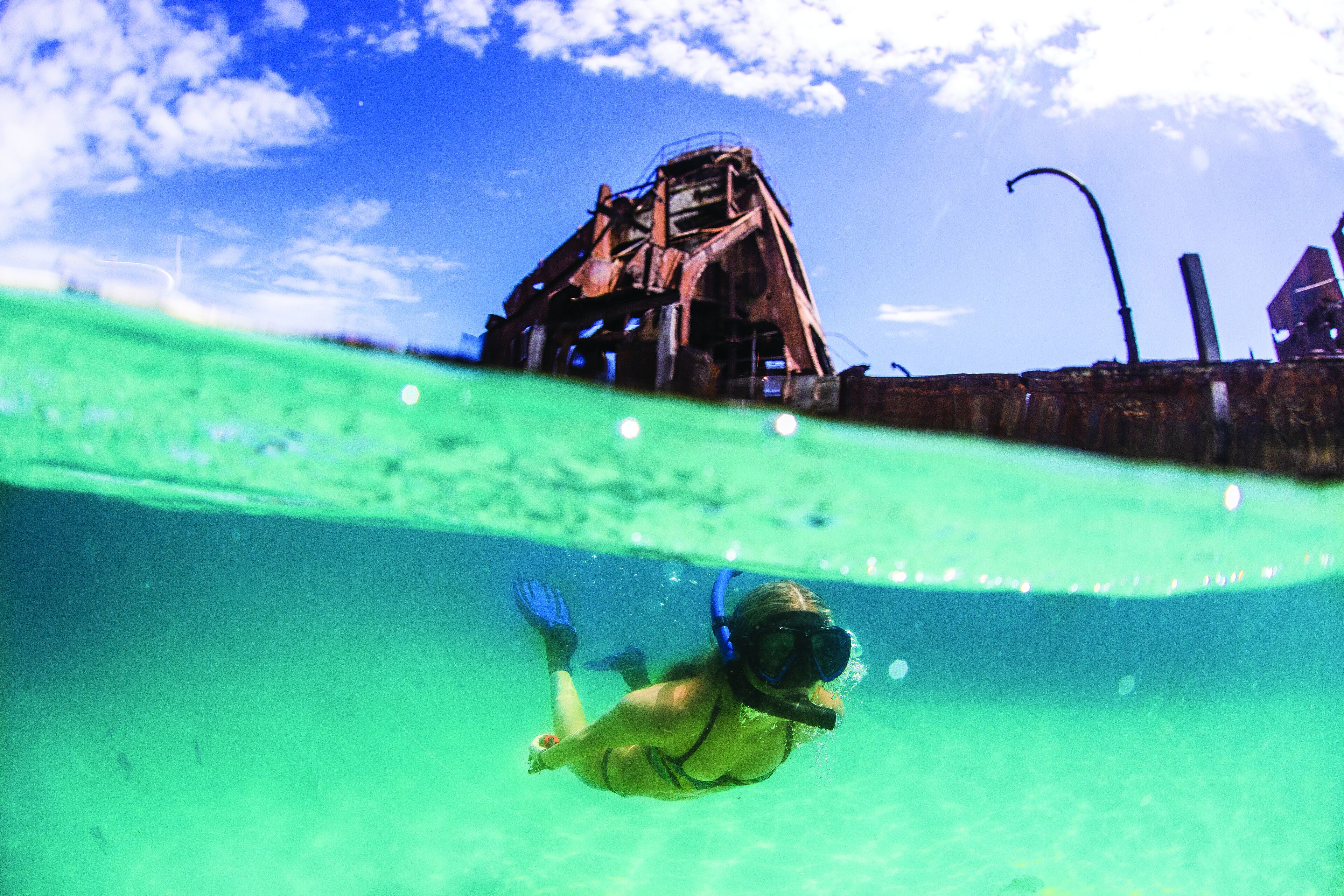 A person snorkeling underwater with a clear view of a rusty structure above the water.