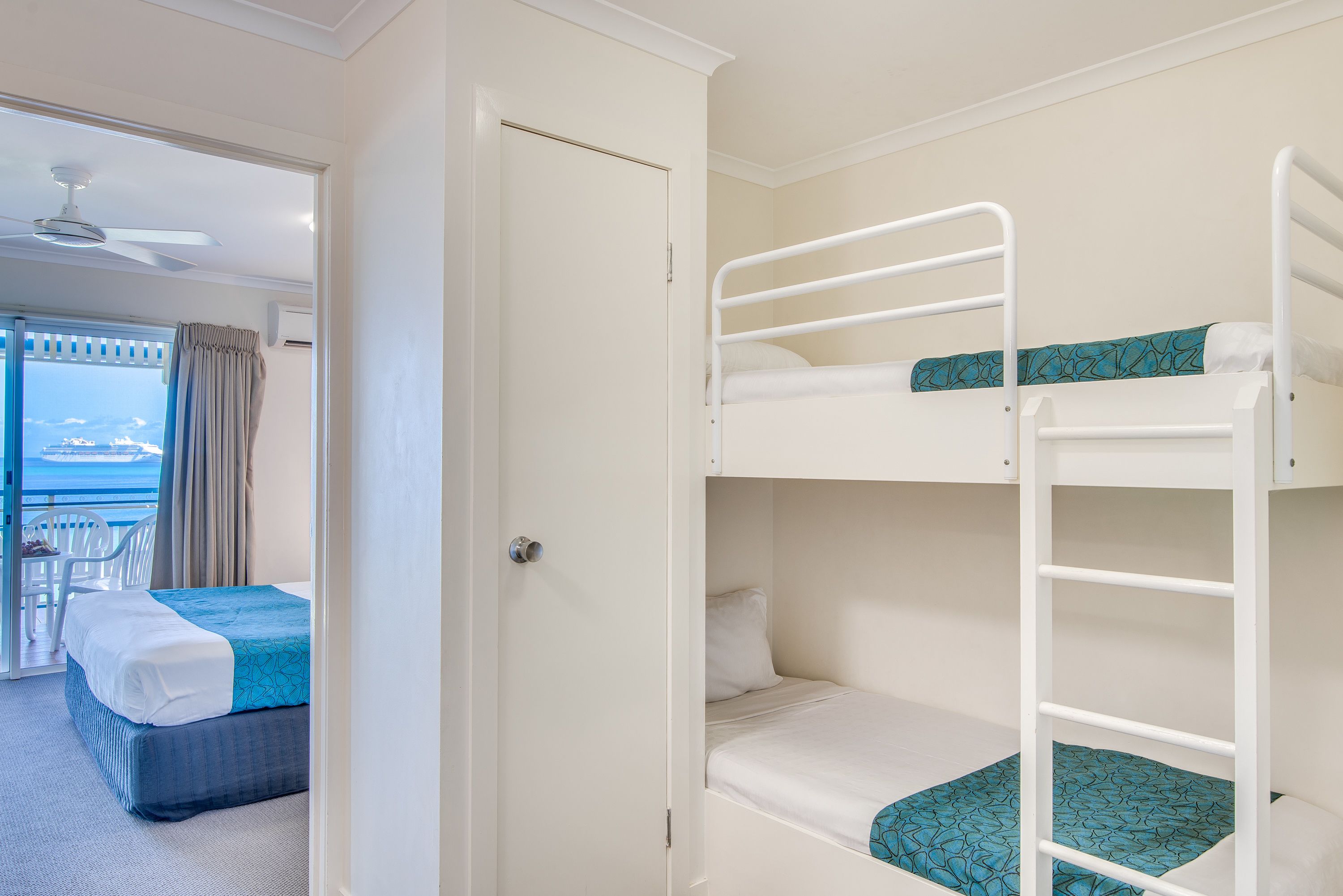 A room with a bunk bed, a single bed, and a balcony with a view.