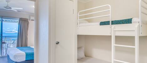A room with a bunk bed, a single bed, and a balcony with a view.