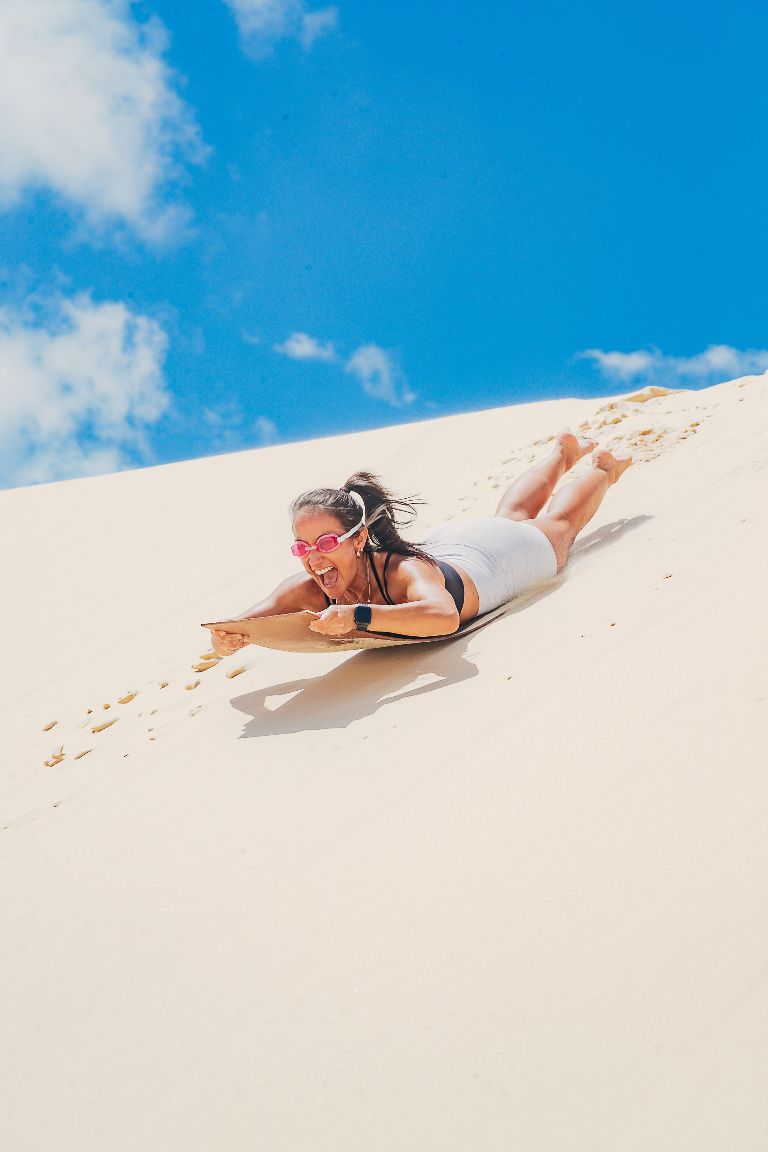A person lying on a sandy surface with a clear blue sky in the background.