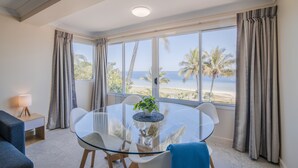 A modern room with a glass table, white chairs, a small plant, and a view of the beach. - Tangalooma Island Resort (Moreton Island)