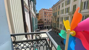 Un balcon doté d’une rambarde en métal surplombe une rue bordée de bâtiments aux couleurs vives, et on peut y voir une enseigne indiquant « Caff. Briston ».