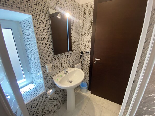 A bathroom with a white sink, a mirror, and a toilet. There is a door on the right side.