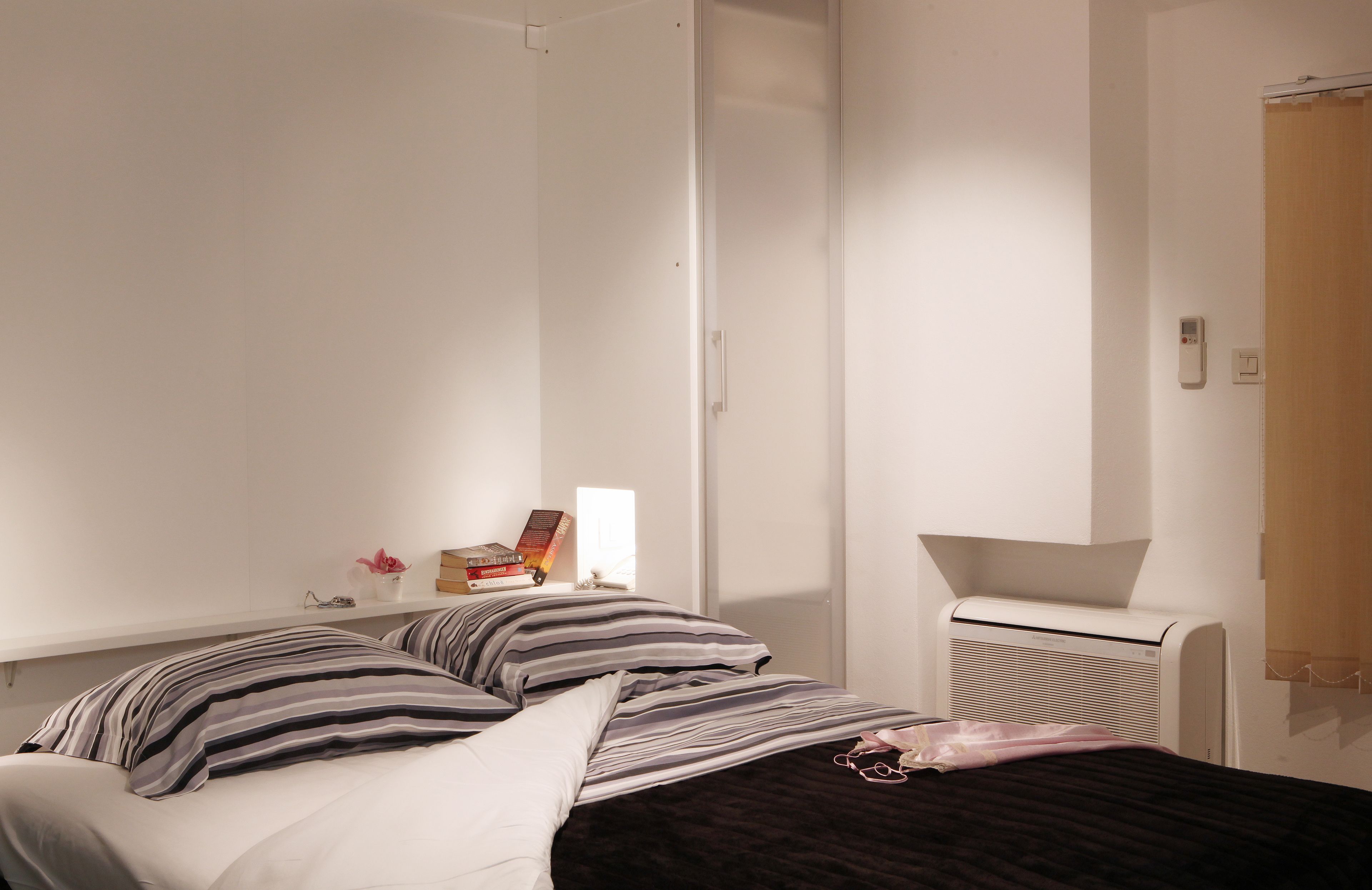 A bedroom with a bed, bedside table, and a wall-mounted heater.