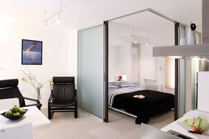 Quarto de hotel moderno com uma cama, uma escrivaninha com um laptop, uma cadeira e uma área de refeições com uma tigela de maçãs.