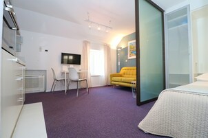 Una habitación de hotel con una cama, un escritorio con silla, un televisor y un sofá.