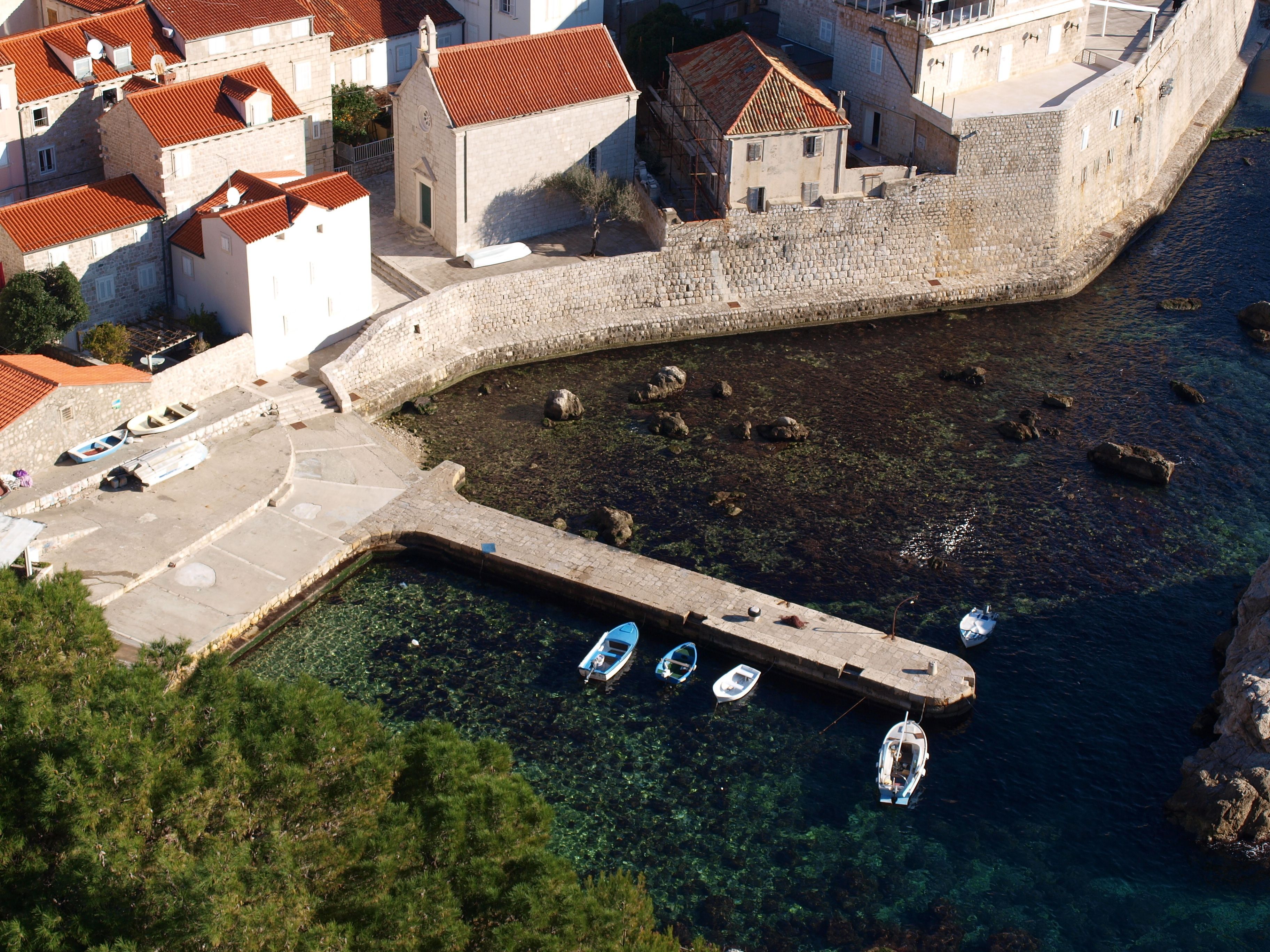 A coastal town with stone buildings, a clear harbor, and boats docked.