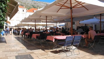Un café en plein air avec des tables et des chaises placées sous des parasols blancs, le tout sur fond de paysage montagneux.