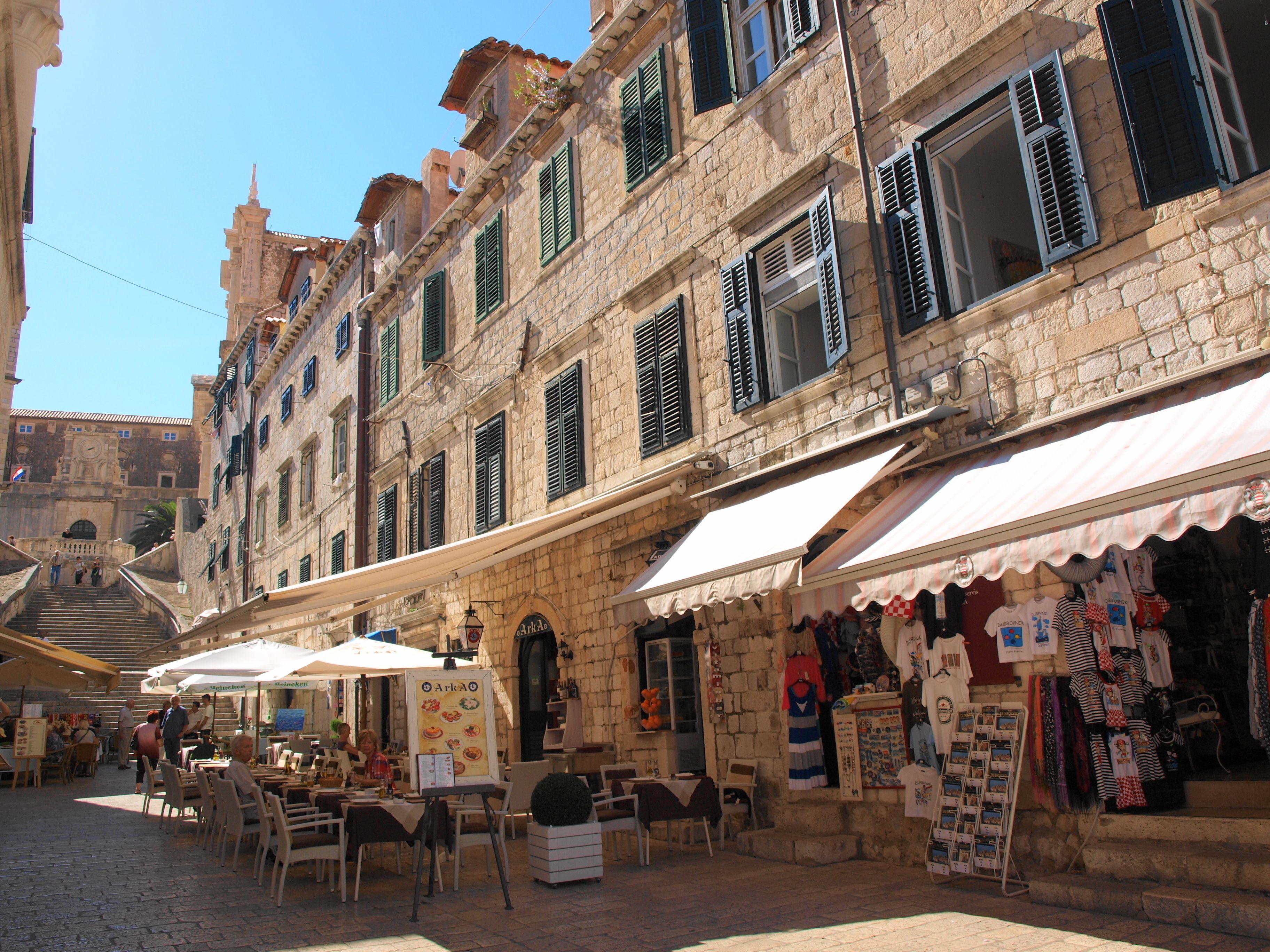 Une rue pavée bordée de terrasses, de bâtiments en pierre et de divers commerces.