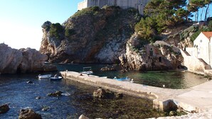 Una fortaleza de piedra histórica en un risco escarpado con vista a un puerto tranquilo donde hay barcos amarrados.