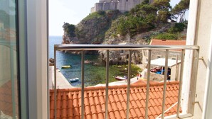 Un balcón con vistas a la costa, incluyendo un castillo en un acantilado y barcos en el agua.