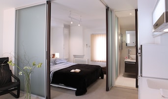 A modern hotel room with a bed, a desk, a chair, a bathroom, and a refrigerator.