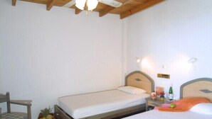 A small, clean room with two single beds, a wooden chair, and a small table with a basket of fruit. - Phoenix Apartments (Agios Vasileios)