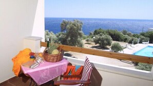 A balcony with a view of the sea, a table with a pink tablecloth, and a wicker basket with fruits. - Phoenix Apartments (Agios Vasileios)