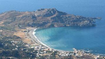An aerial view of a coastal town with a prominent mountain, clear blue waters, and a mix of residential and natural areas.