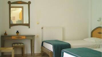 A room with a wooden desk, a mirror, a radiator, and two single beds with blue bedding.