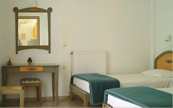 Una habitación con un escritorio de madera, un espejo, un radiador y dos camas individuales con ropa de cama azul.