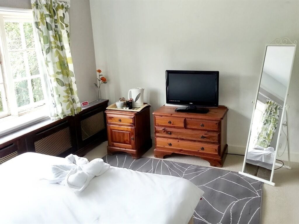 A hotel room with a bed, a TV on a wooden dresser, a mirror, and a window with curtains.