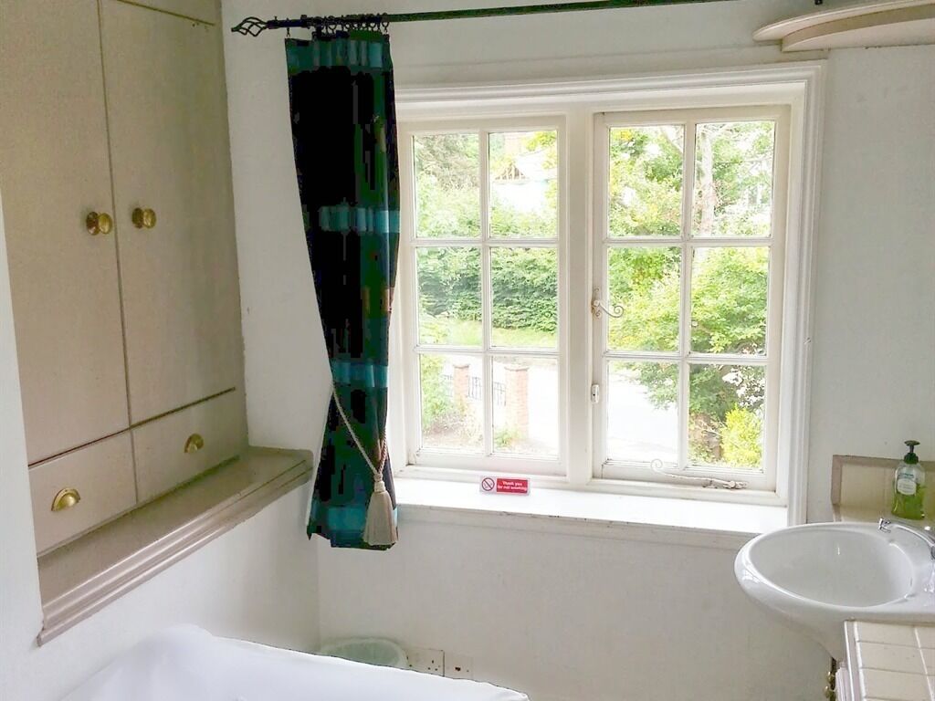 A bathroom with a bathtub, a window with a view of greenery, and a sink.