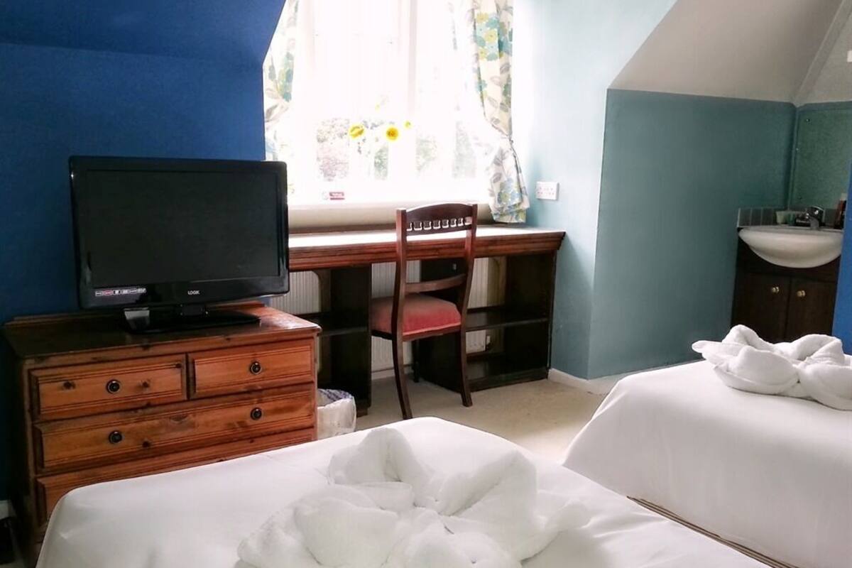 A hotel room with a bed, a desk with a television, a chair, and a bathroom with a sink.