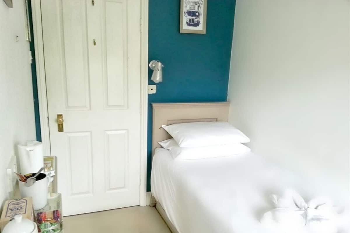 A small, neatly made bed in a room with a white door and teal walls.