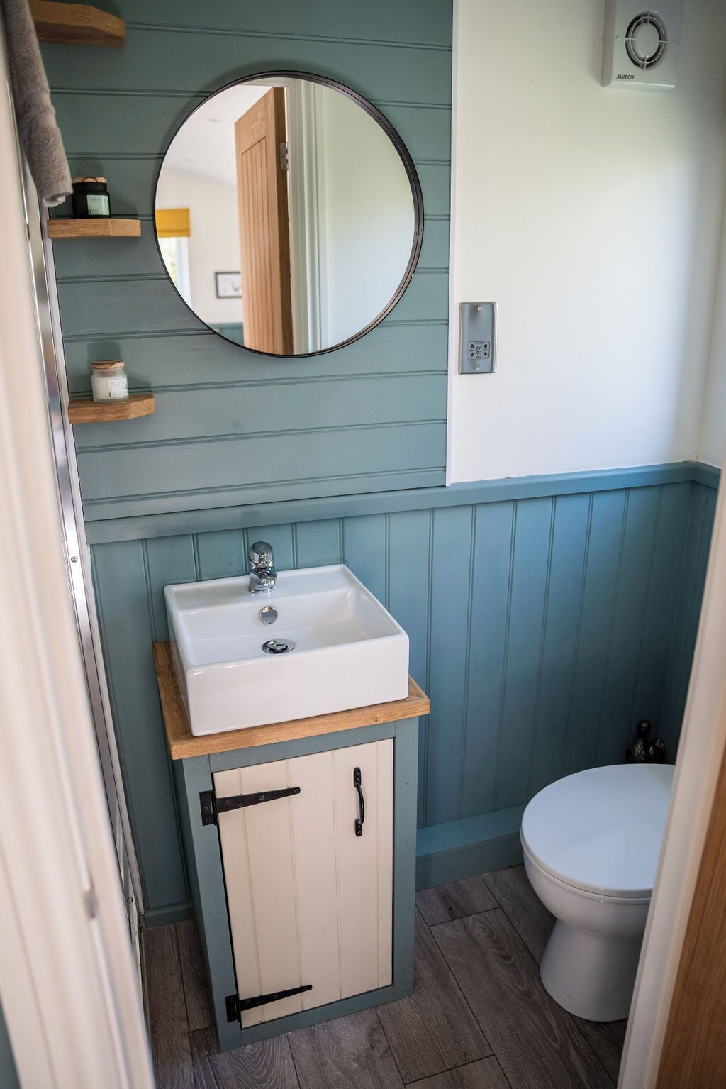 A compact bathroom with a white sink, a round mirror, and a toilet.