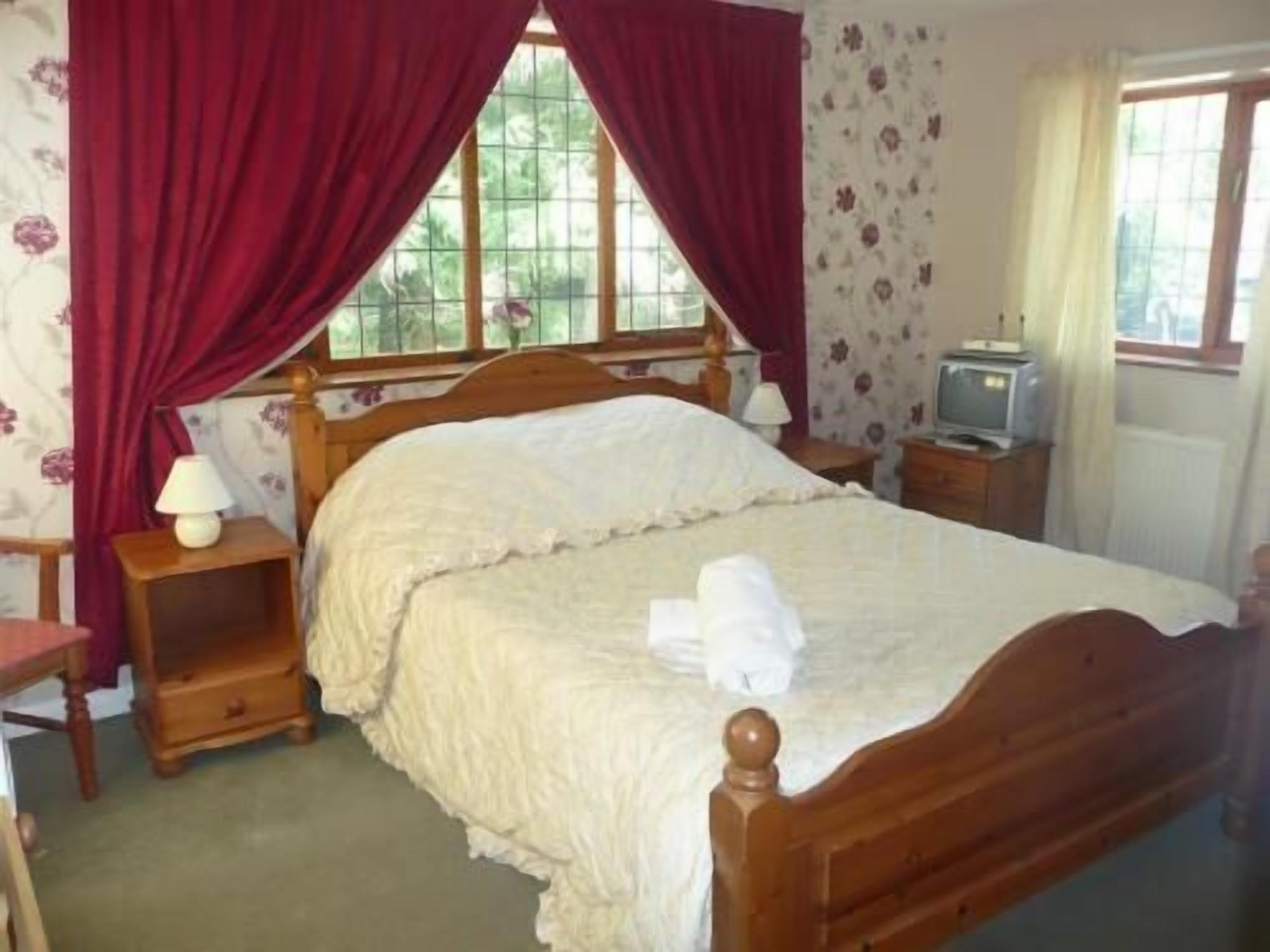 Une chambre à coucher avec un lit en bois, une table de chevet avec une lampe, une commode et un téléviseur posé sur une petite table d’appoint.
