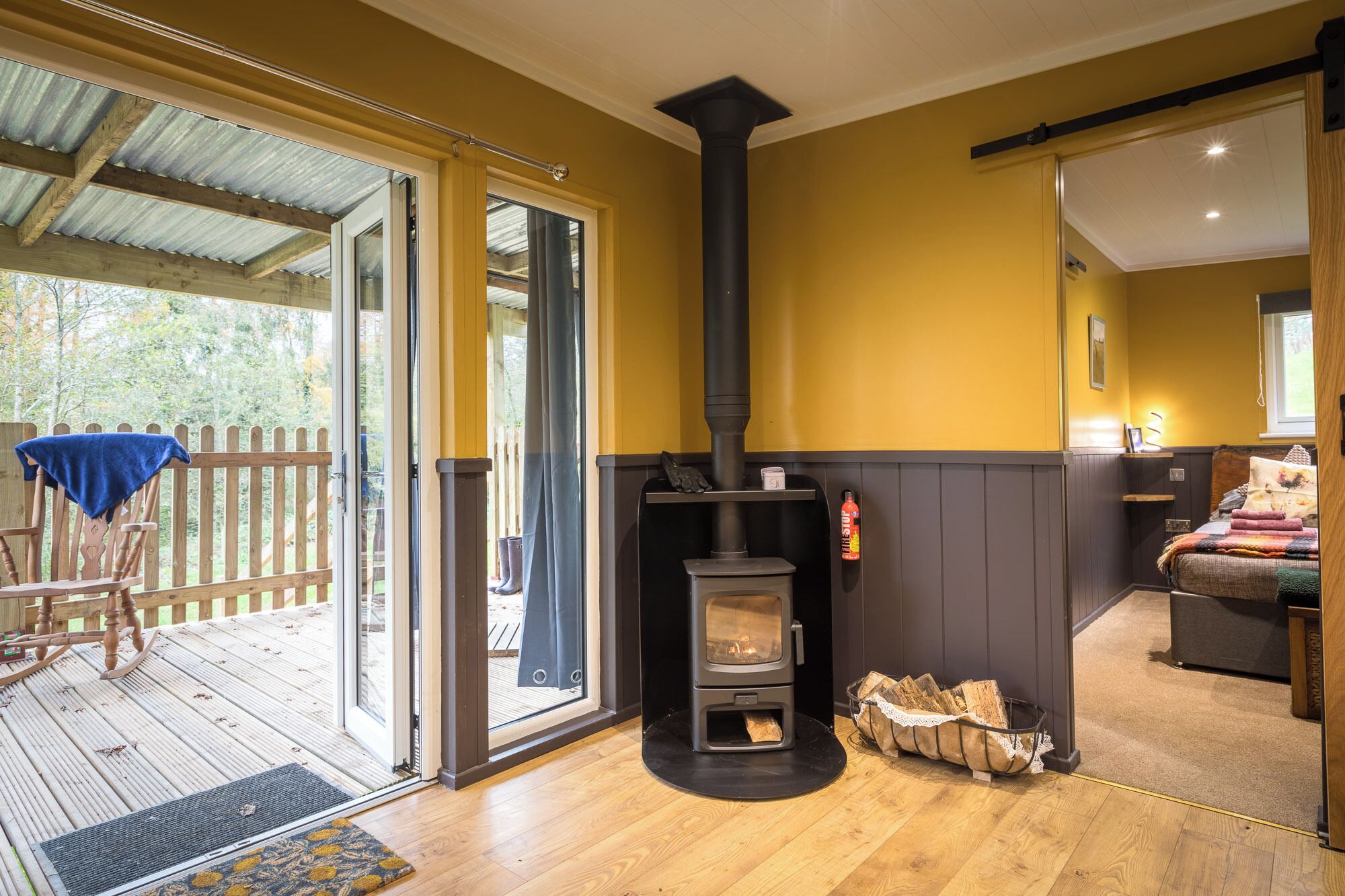 A cozy room with a wood-burning stove, a wooden deck, and a sliding glass door leading to an outdoor area.