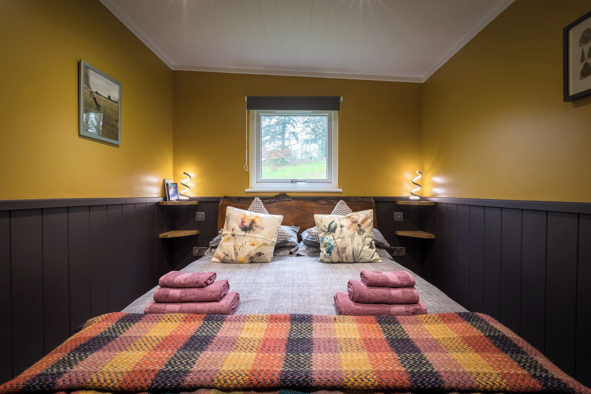 Une chambre avec un lit, deux tables de chevet, une fenêtre et une vue sur les arbres.