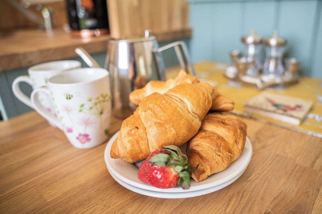 A wooden table with croissants, a strawberry, and a floral mug.