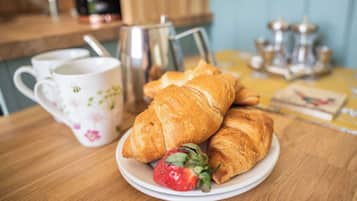 A wooden table with croissants, a strawberry, and a floral mug.