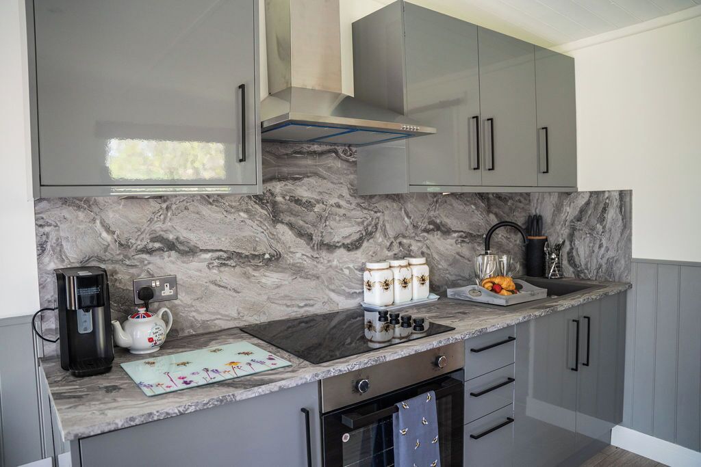 A modern kitchen with grey cabinets, a marble backsplash, a built-in oven, and a coffee machine.