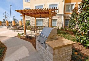 Un patio exterior con una parrilla, zona de estar y una piscina al fondo.