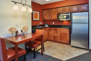 Una cocina compacta con armarios de madera, un refrigerador de acero inoxidable, un microondas y una mesa de comedor con sillas.