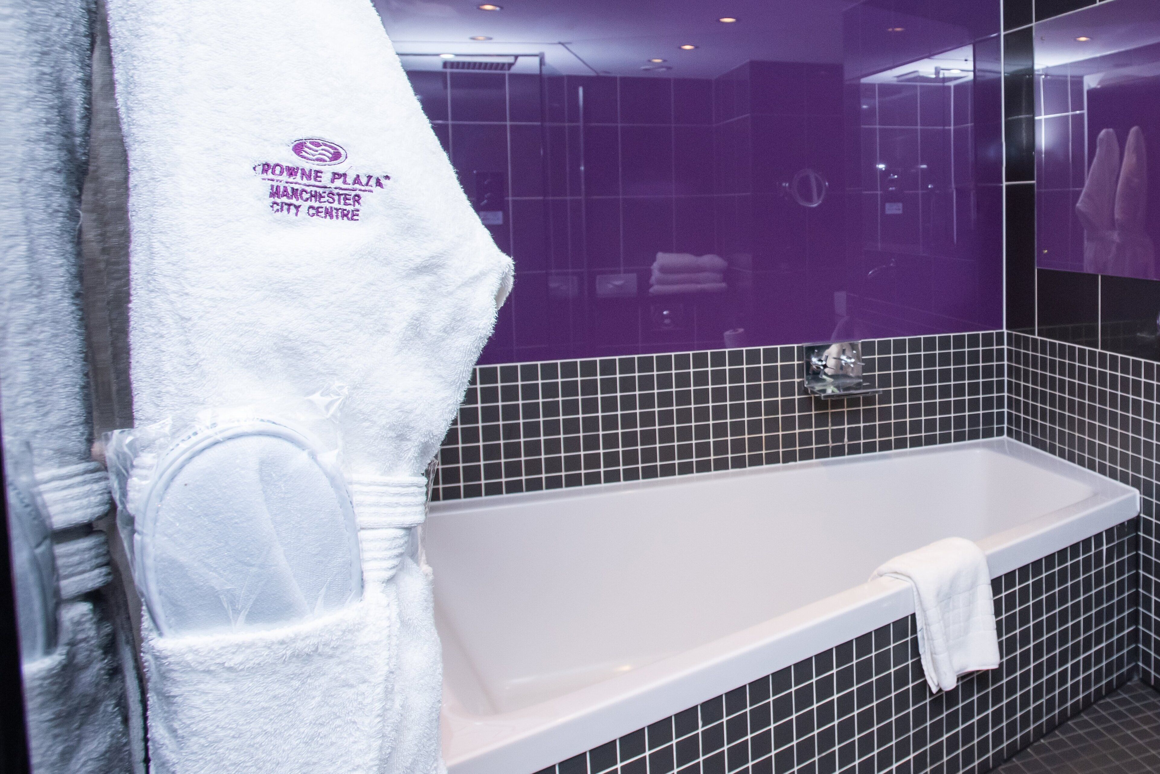 Une salle de bain moderne avec une baignoire blanche, des murs recouverts de carreaux noirs et une serviette blanche accrochée au mur.