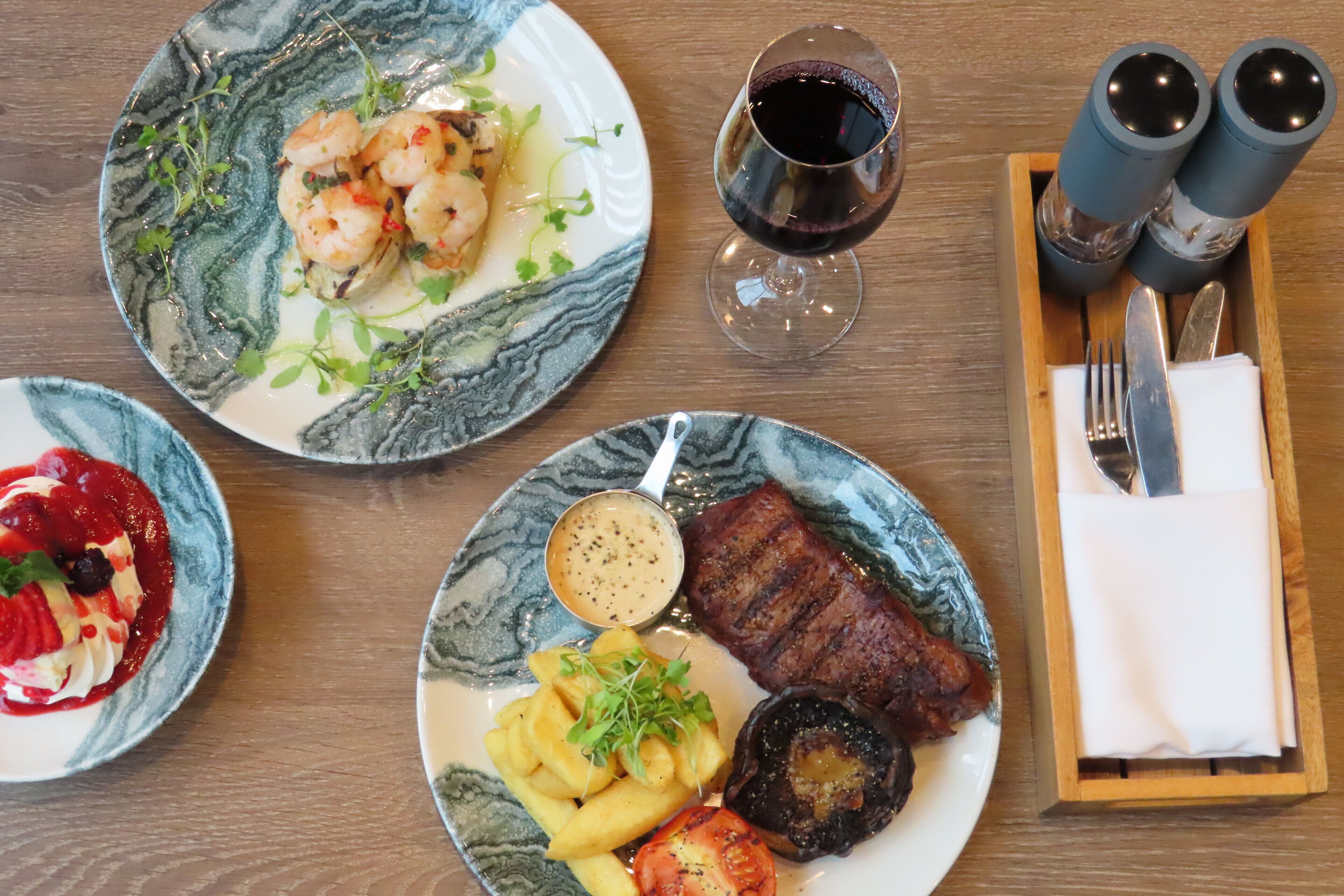 Une table à manger avec des assiettes remplies de nourriture, un verre de vin rouge et un ensemble de salière et de poivrière.
