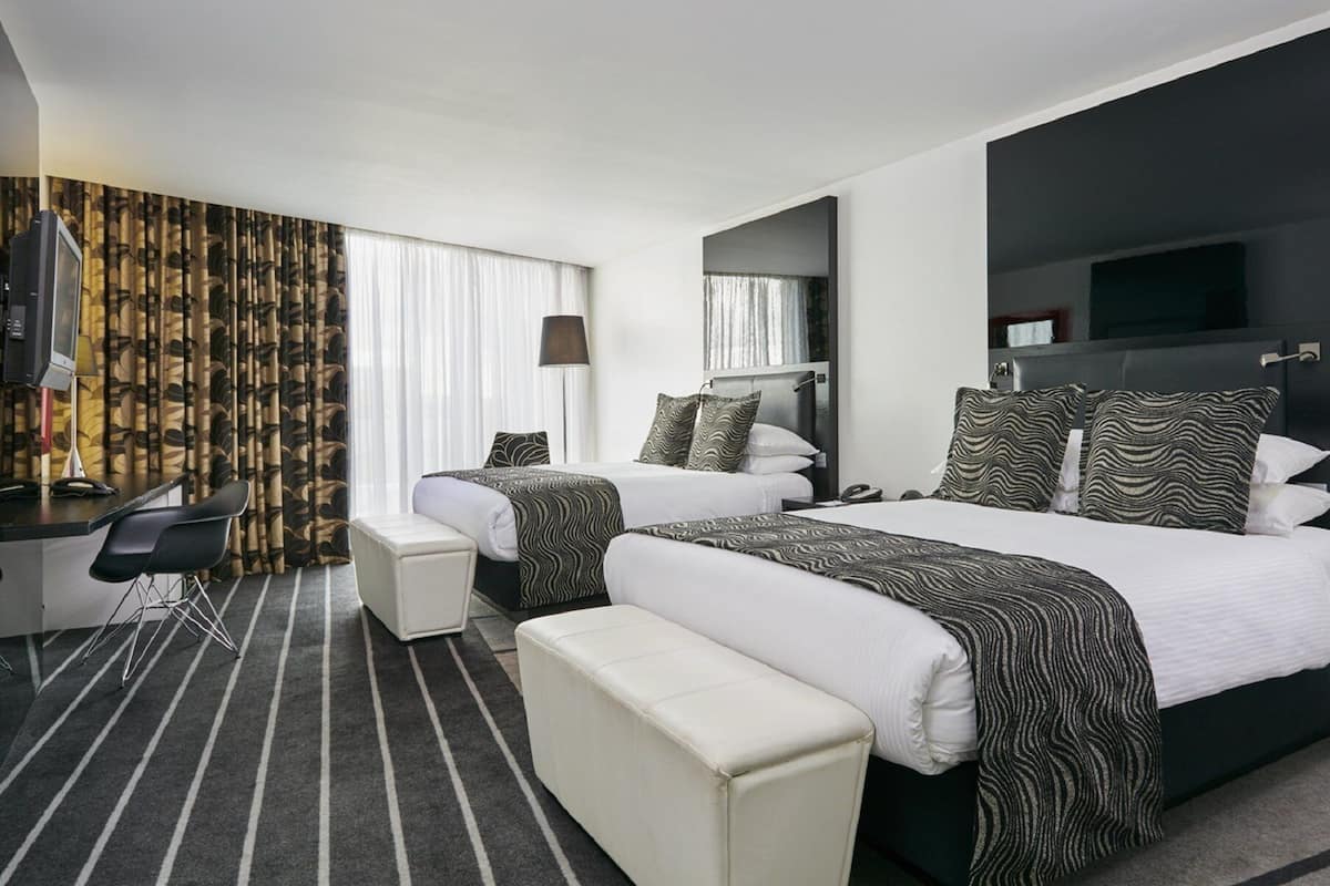Een hotelkamer met twee bedden, een bureau, een stoel, een bankje en een televisie.