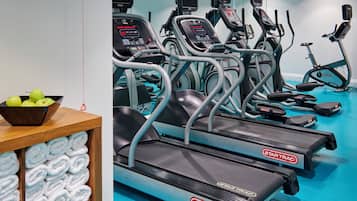 Un gimnasio con varias cintas de correr, bicicletas estáticas y una mesa de madera con toallas y manzanas.