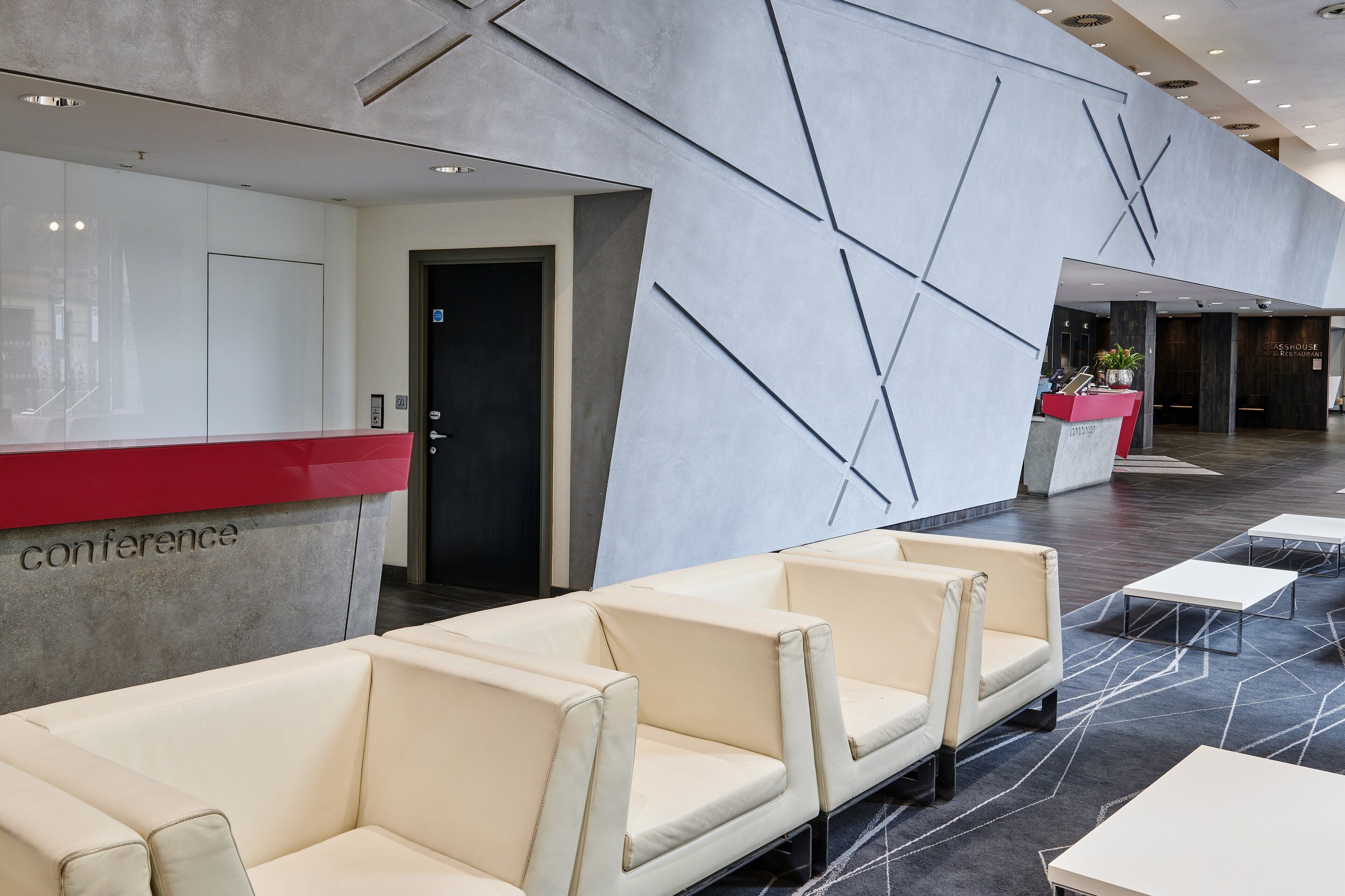 A hotel lobby with a reception desk, seating area, and a glasshouse bar.
