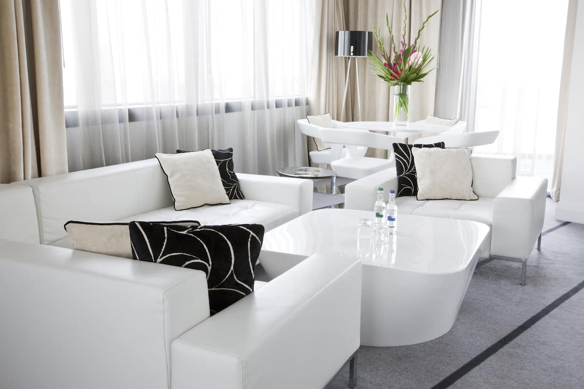 Een moderne hotelkamer met een witte zithoek, een ronde salontafel en een bijzettafeltje.