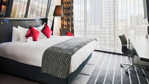 Ein Hotelzimmer mit einem großen Bett, einem Schreibtisch und Blick auf die Stadt.
