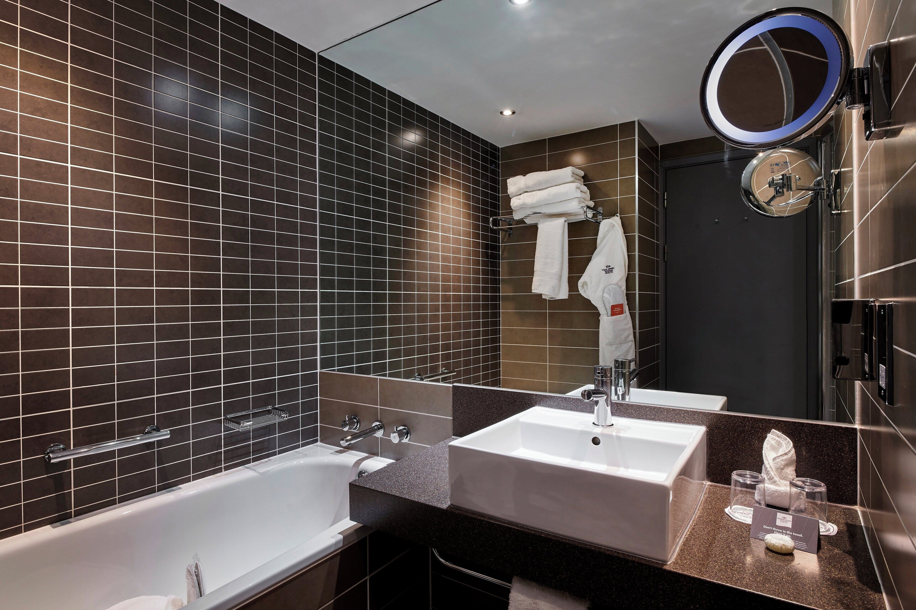 A modern bathroom with a bathtub, two sinks, a mirror, and a towel rack.