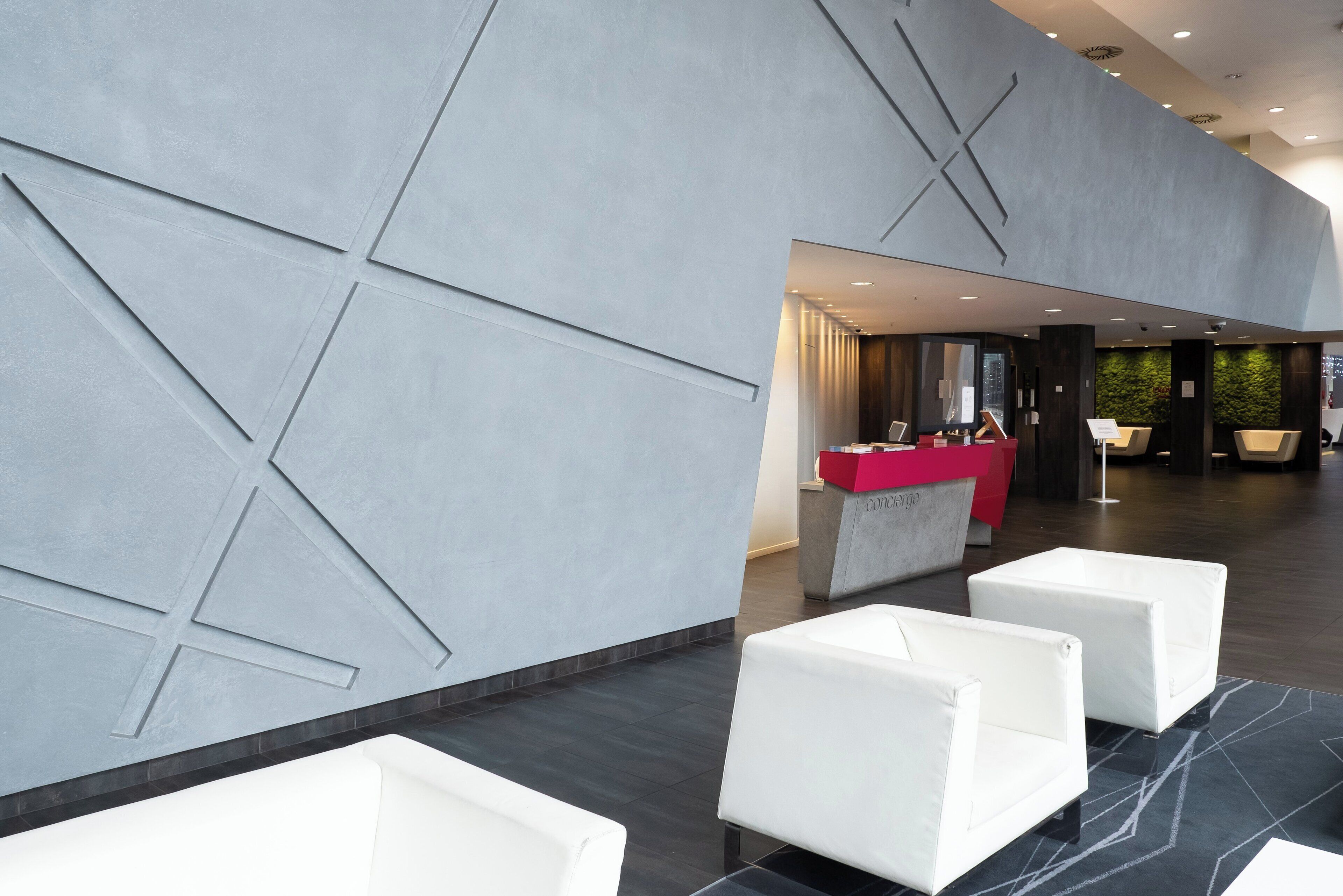 Um lobby moderno com padrões geométricos nas paredes, um balcão de recepção e áreas de estar com assentos brancos.