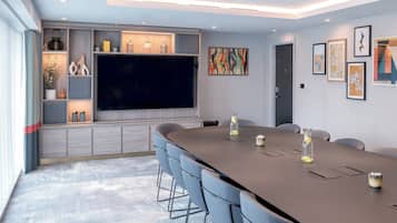 A conference room with a long table, chairs, a large flat-screen TV, and decorative items on shelves.