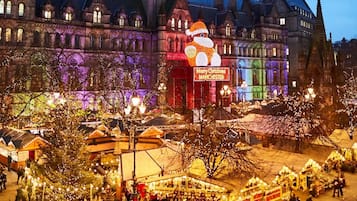 A historic building with a Christmas market in front, featuring illuminated trees and stalls.