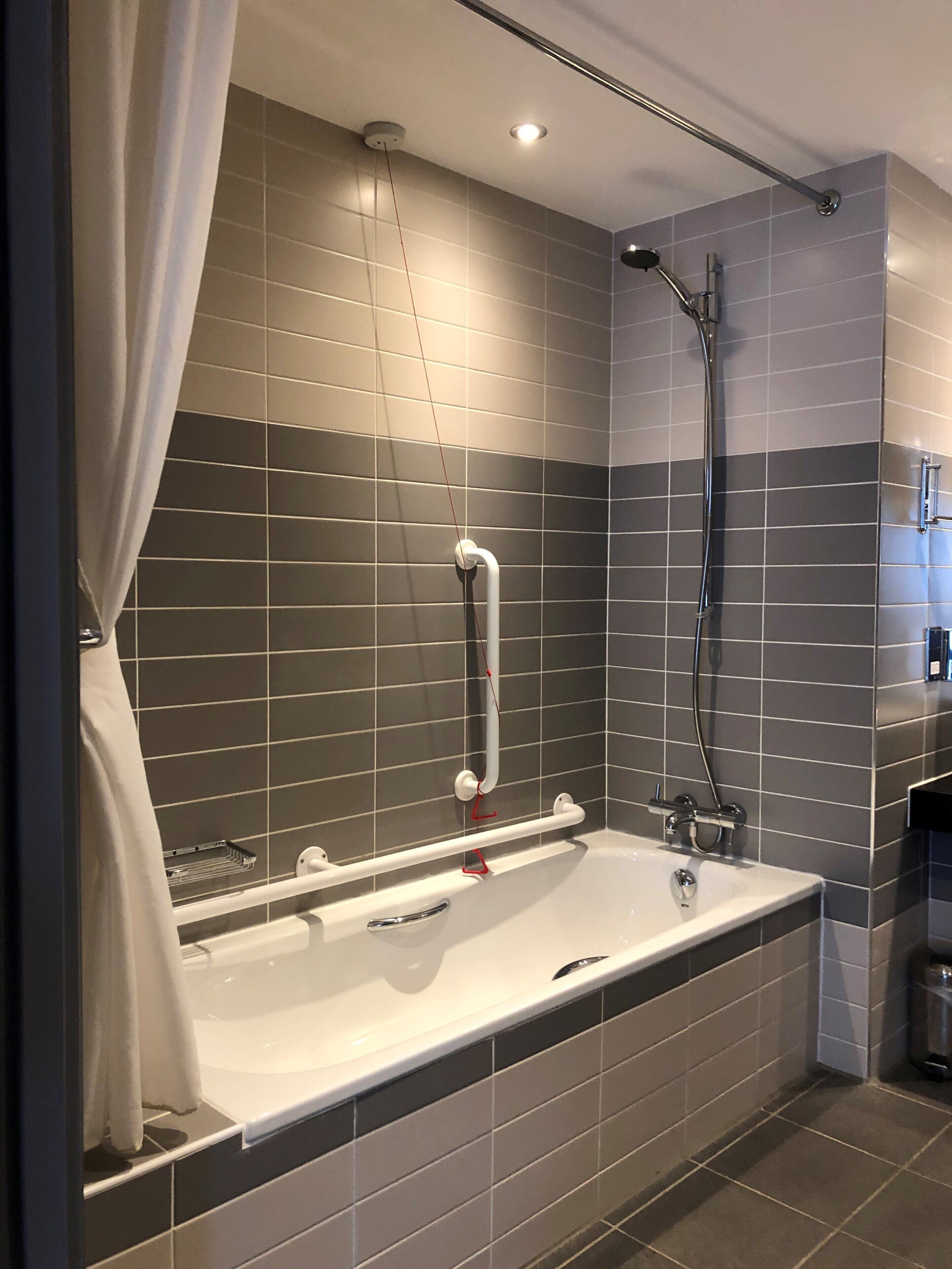 Une salle de bain moderne équipée d’une baignoire, d’une douche et de barres d’appui.