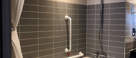 Une salle de bain moderne équipée d’une baignoire, d’une douche et de barres d’appui.