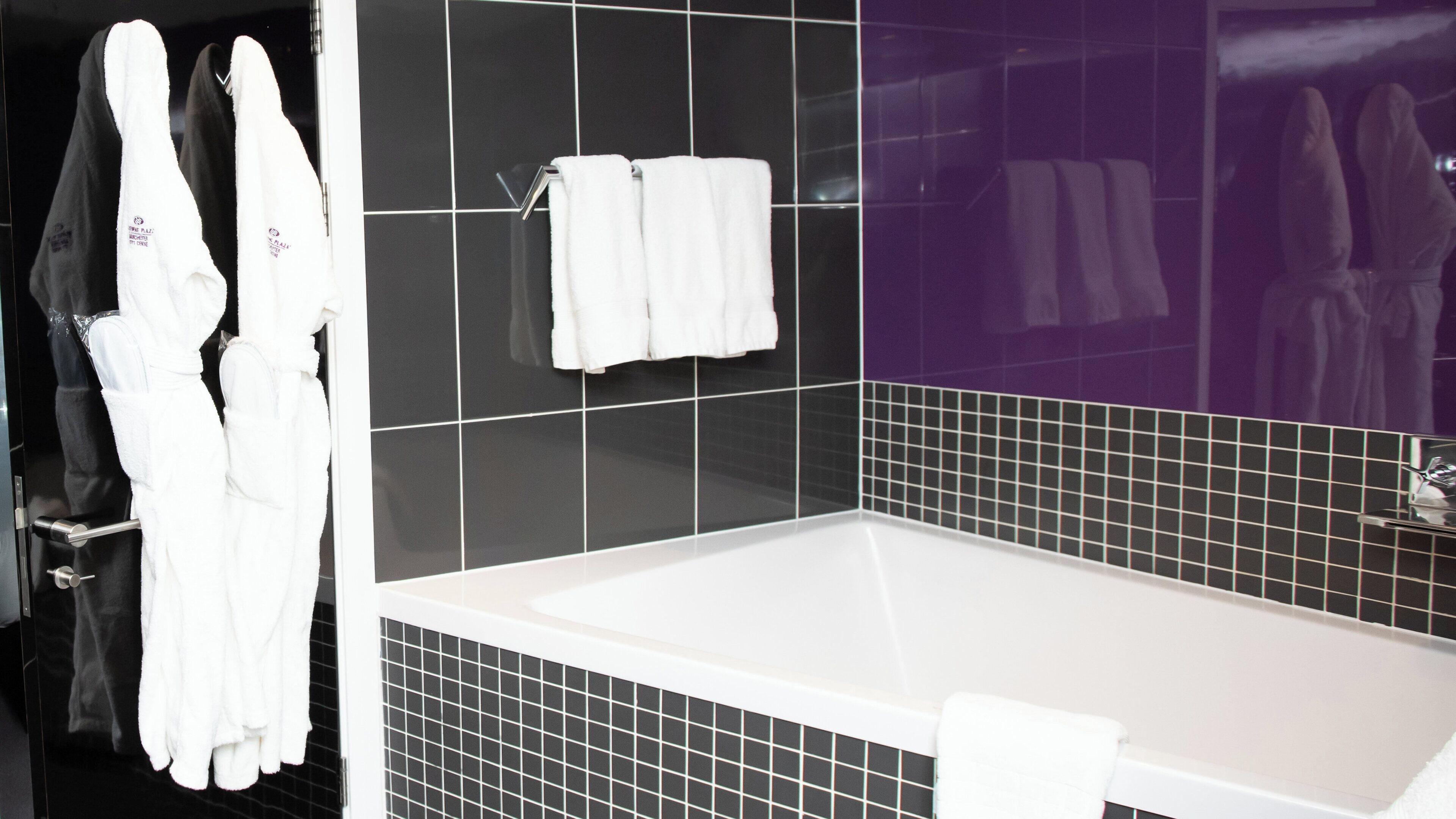 Un baño con bañera, paredes con azulejos blanco y negro y toallas blancas colgadas de ganchos.